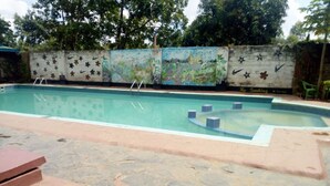 Une piscine avec une terrasse carrelée, une fresque murale et quelques chaises longues.