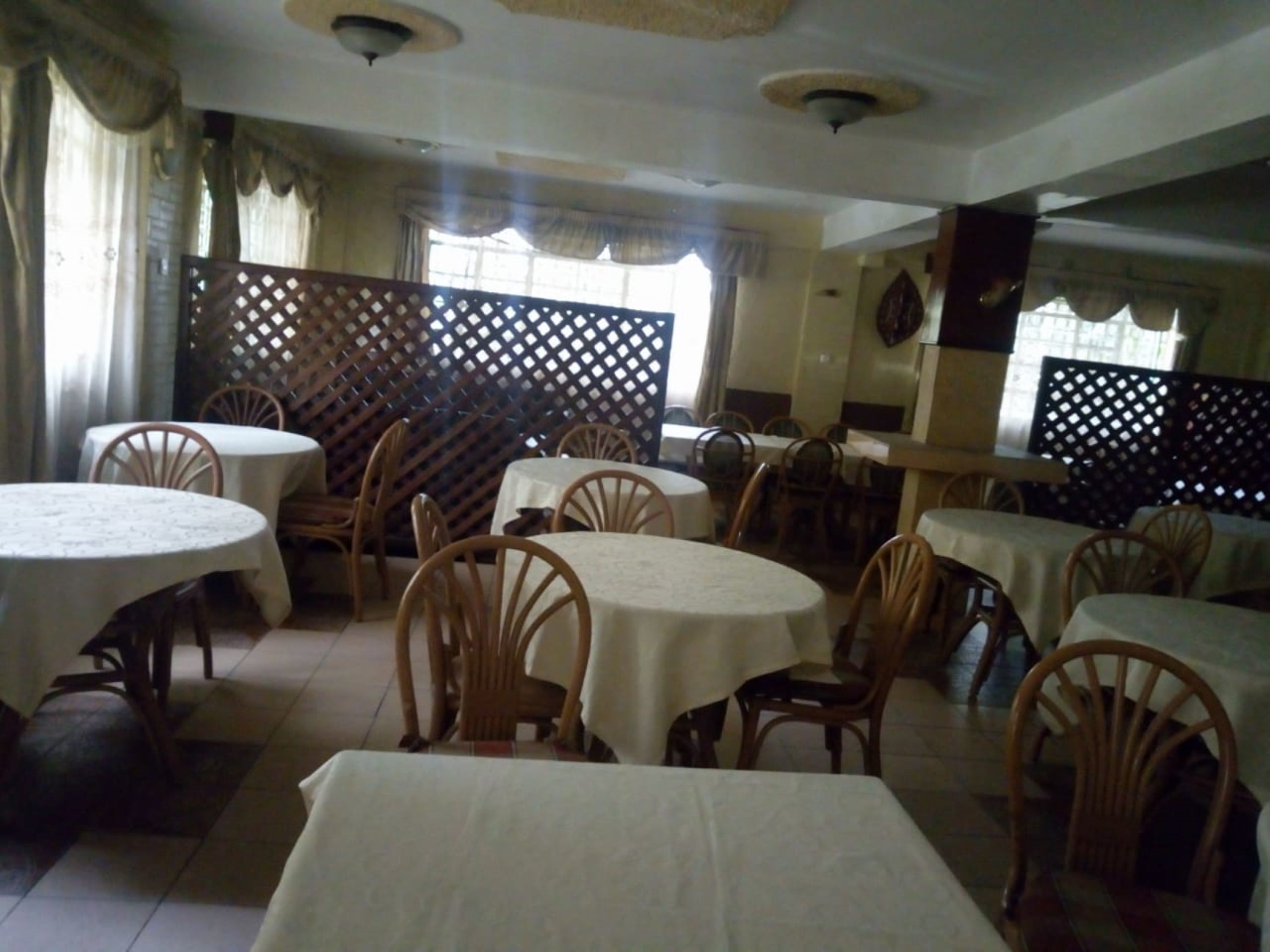 A dining area with round tables and wooden chairs, covered with white tablecloths.