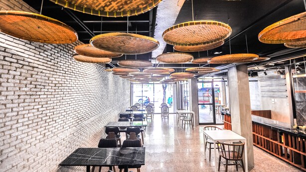 Interior de un restaurante con paredes de ladrillo, lámparas colgantes tejidas y una larga barra con mesas y sillas.