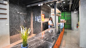 Un área de recepción moderna con una barra de mármol, una planta en maceta y una pared decorativa verde.