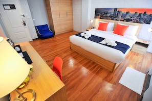 A hotel room with a bed, a desk, a chair, a nightstand, and a wall with a cityscape painting. - 7 Days Premium Hotel at Icon Siam Station (Bangkok)