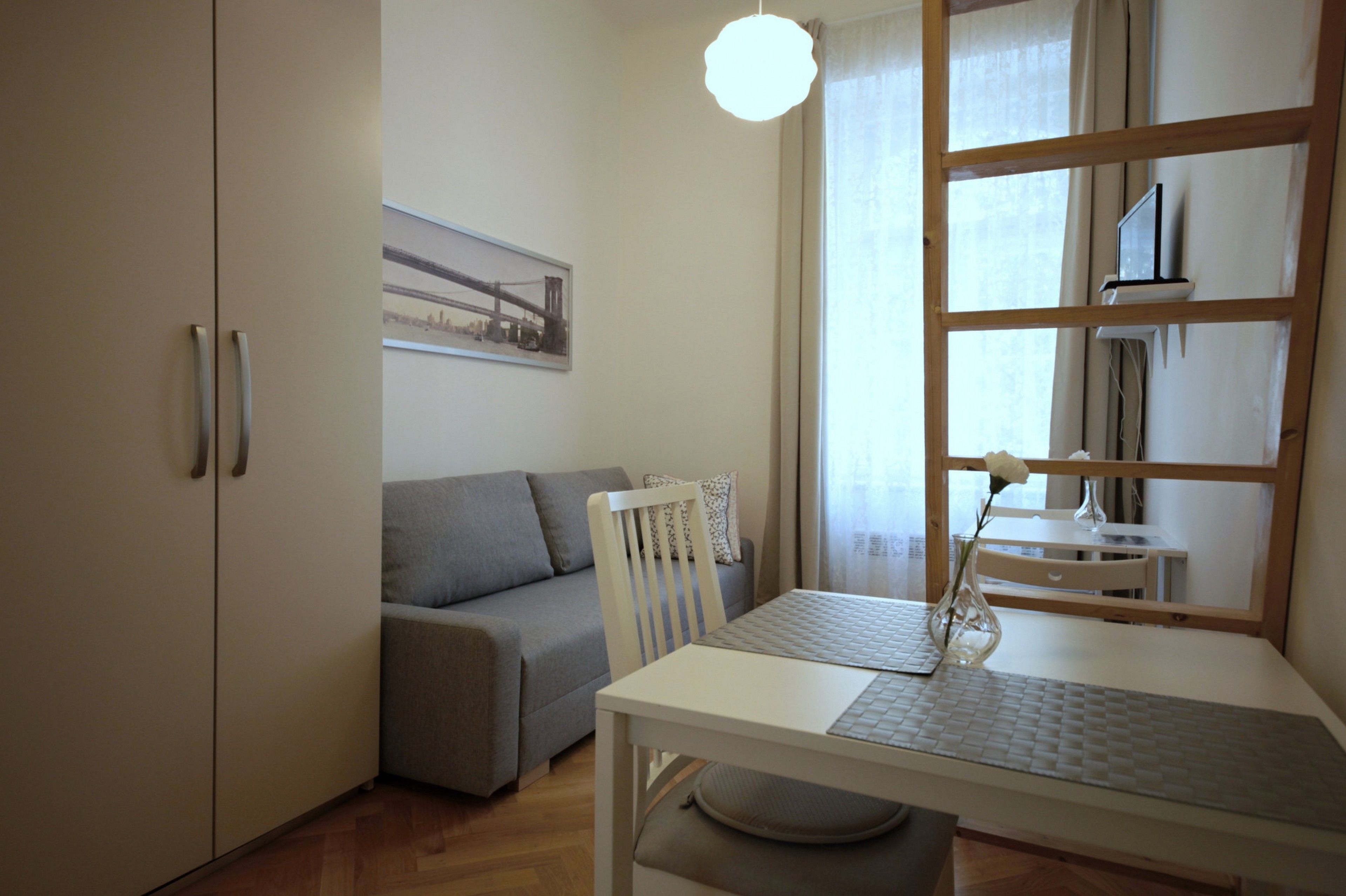 Una habitación moderna con un sofá gris, una mesa de comedor blanca con un florero y un ventanal con cortinas.
