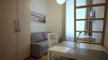 Una habitación moderna con un sofá gris, una mesa de comedor blanca con un florero y un ventanal con cortinas.