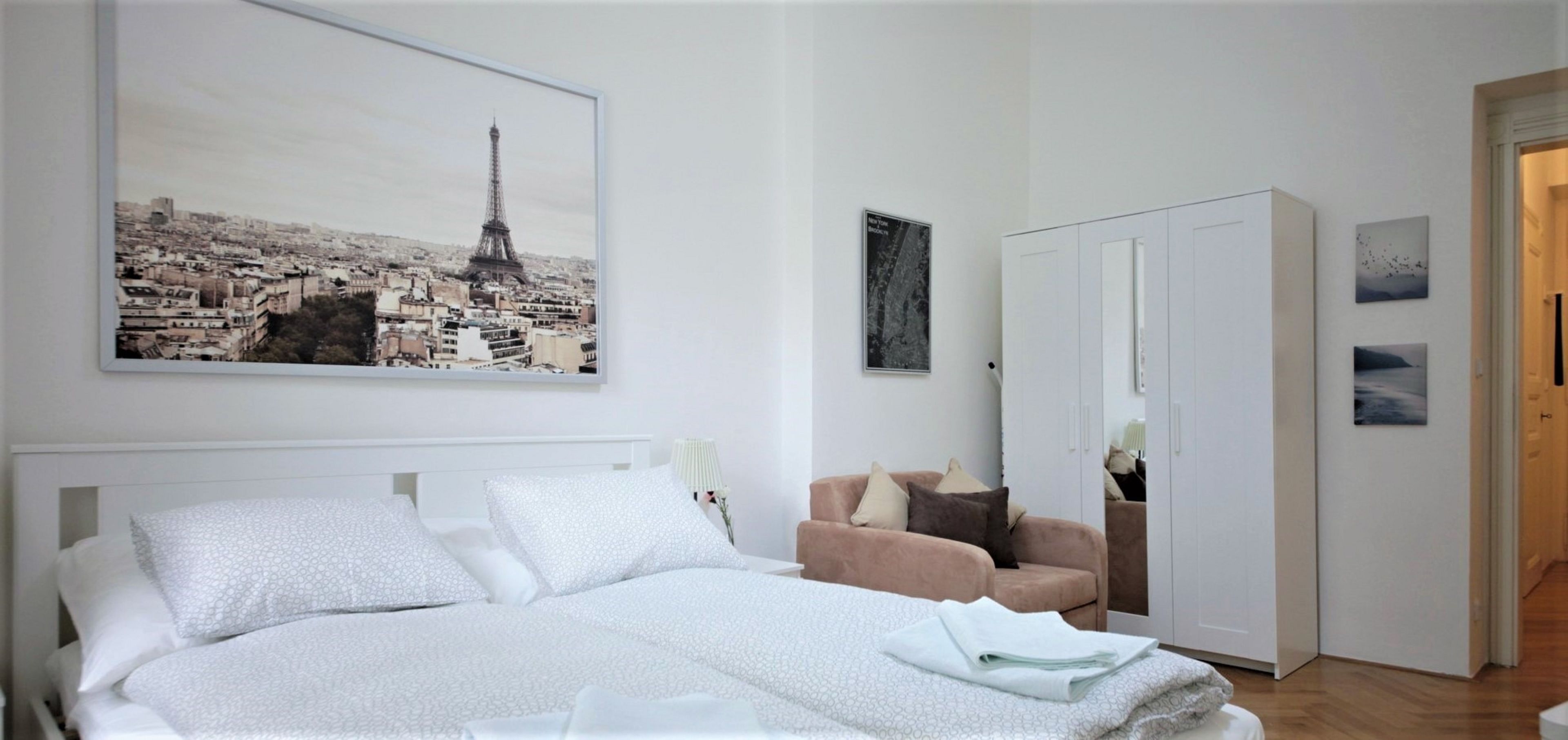 Une chambre à coucher comprenant un lit, un canapé, une armoire et un grand tableau encadré représentant la Tour Eiffel.