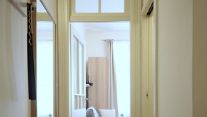 Un pasillo que conduce a un dormitorio con cama, espejo y ventana con cortinas.
