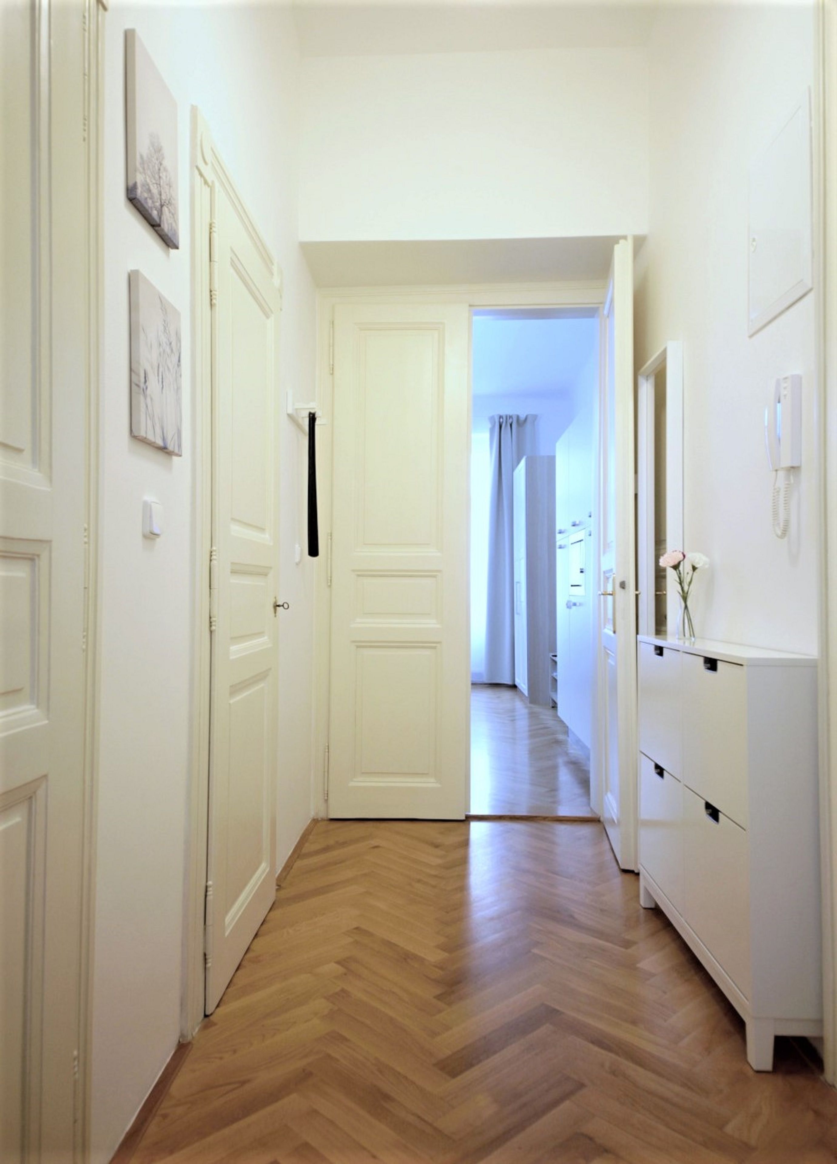 A hallway with wooden flooring, white doors, and a white cabinet with a telephone.