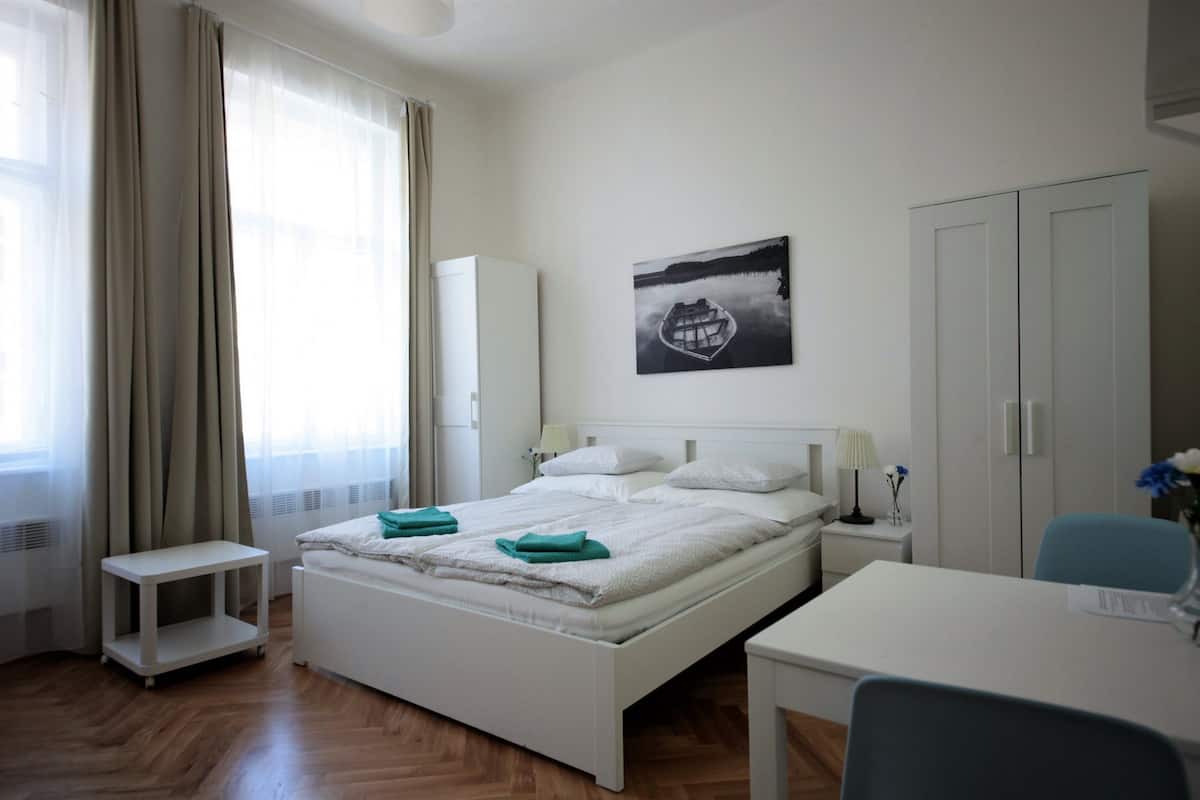 A hotel room with a bed, bedside table, lamp, and a painting on the wall.