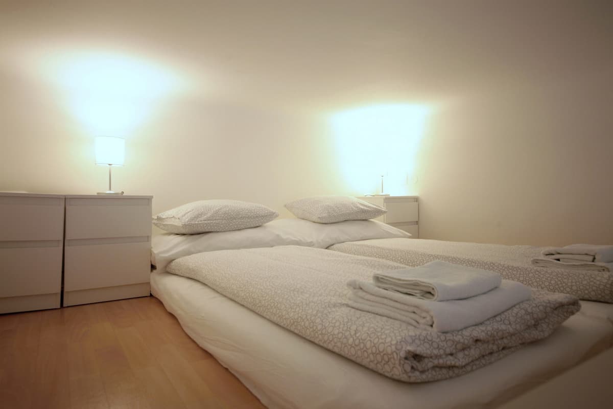 A hotel room with two beds, white bedding, bedside lamps, and a wooden floor.