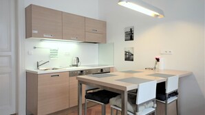 Cocina compacta con lavavajillas integrado, un pequeño comedor con una mesa y sillas, y una lámpara colgante sobre la mesa.