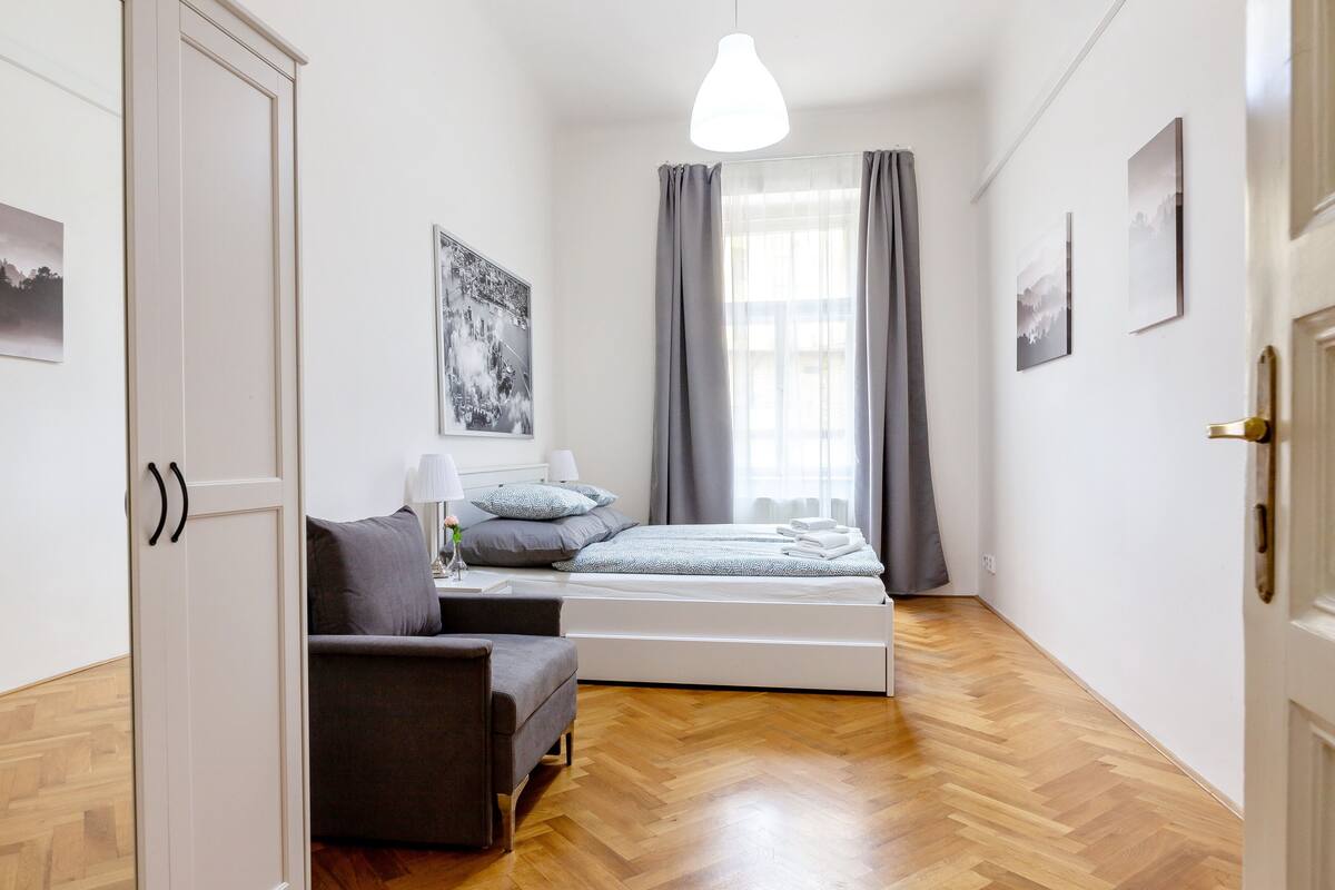 A bedroom with a bed, a chair, a nightstand, and a window with curtains.