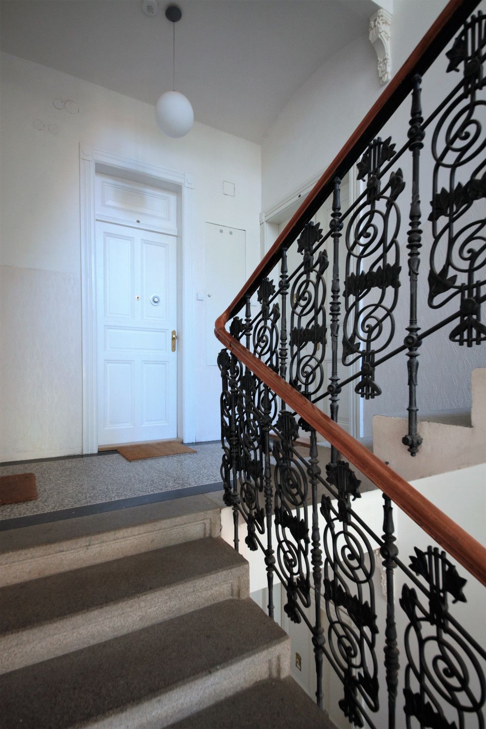 A staircase with a wooden handrail and ornate black metal balusters.