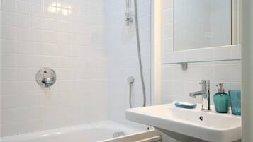 Un baño moderno con paredes de azulejos blancos, una bañera blanca, un lavabo con espejo y un inodoro.