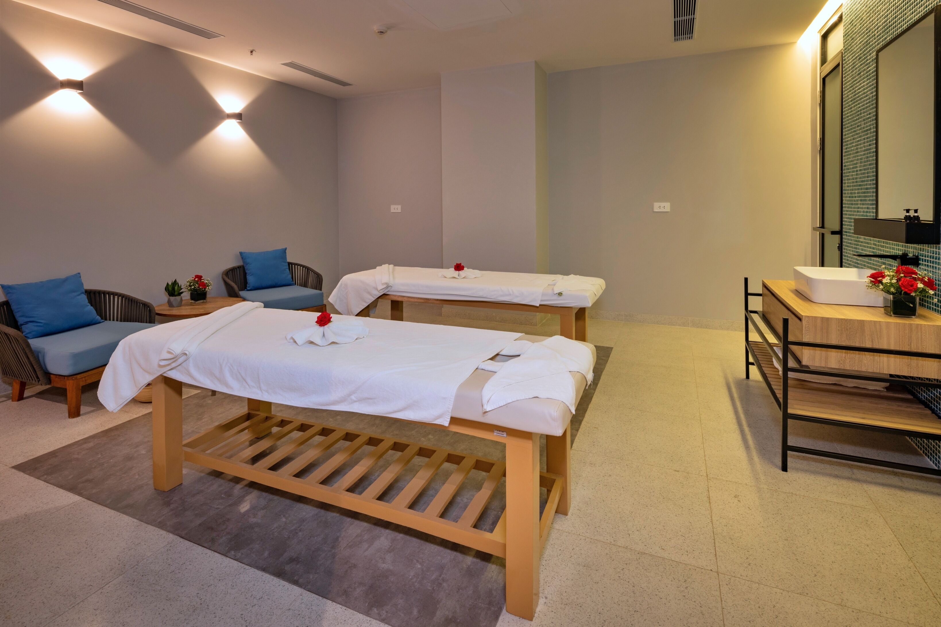 A spa room with two massage tables, a wooden bench, a small sofa, and a vanity with a mirror and sink.
