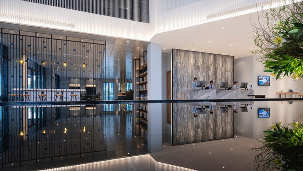 A modern hotel lobby with a reflective floor, a reception desk, seating area, and a large plant. - Anya Beach Hotel Quy Nhon (Quy Nhon Nam)