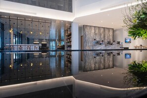 Un moderno vestíbulo de hotel con piso reflectante, un mostrador de recepción, zona de estar y una planta grande.