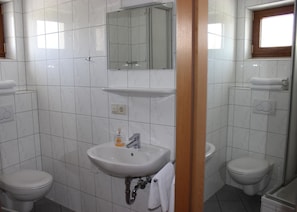A bathroom with white tiled walls, a sink, a mirror, two toilets, and a window.