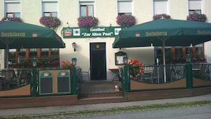 Ein Gebäude mit einem Schild, auf dem „Gasthof Zur Alten Post“ und „Harklberg“ stehen, und grünen Sonnenschirmen.
