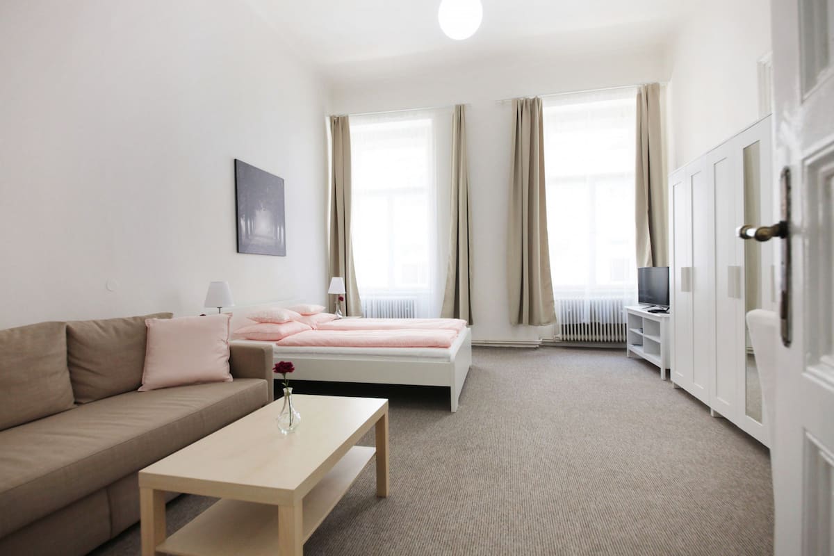 A modern hotel room with a bed, a sofa, a coffee table, a TV, and a radiator.