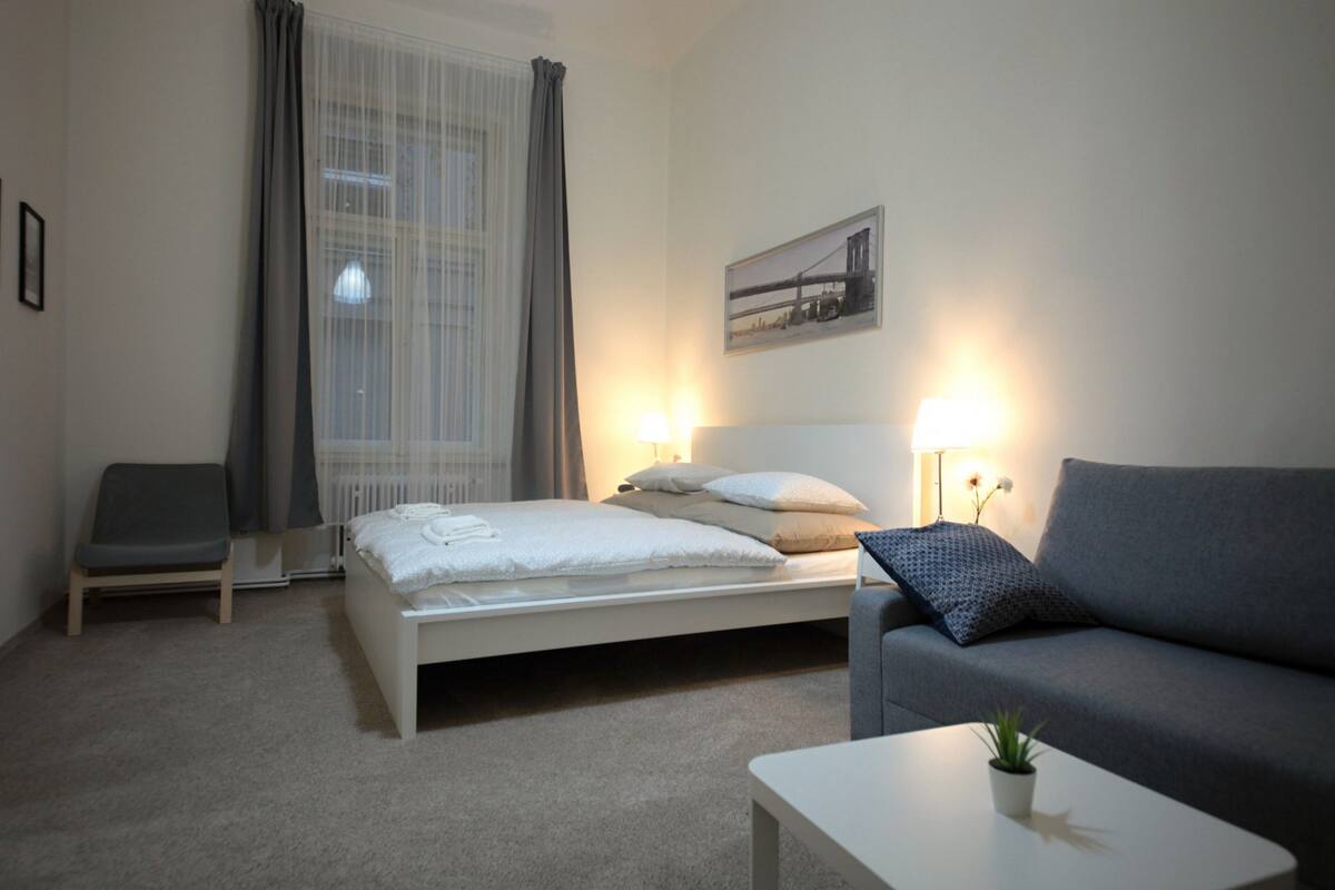 A hotel room with a bed, a sofa, a chair, a small table, and a window with curtains.