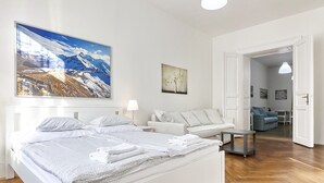 A modern hotel room with a large bed, a sofa, and a dining table. There is a painting of a mountain landscape on the wall and a door leading to another room. - Aparthotel Wenceslas (Prague)