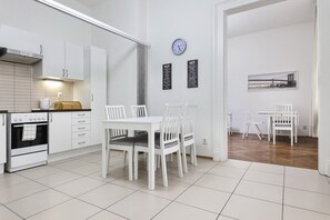 A modern kitchen with white cabinetry, a built-in oven, and a dining area with a white table and chairs. There is a clock on the wall and a framed picture above the dining table. - Aparthotel Wenceslas (Prague)