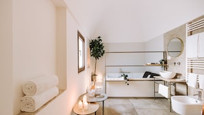 A modern bathroom with a bathtub, a sink, and a vanity. There are towels on the wall and a small table with candles. - Suite1212 Pirrelli (Monopoli)