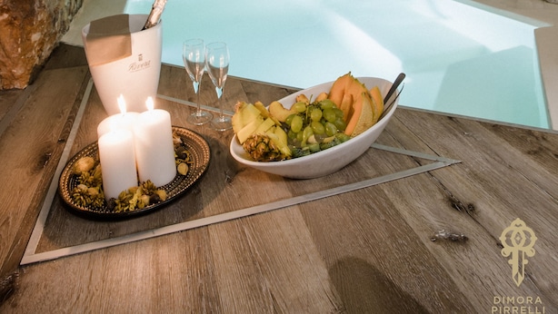 A stone-walled room with a bathtub, candles, and a fruit bowl on a wooden table. - Suite1212 Pirrelli (Monopoli)