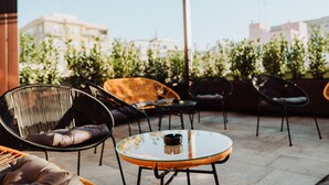 An outdoor patio with wicker chairs and a glass table, surrounded by greenery and buildings in the background. - Suite1212 Pirrelli (Monopoli)