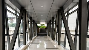 Un couloir doté d’un sol carrelé réfléchissant, de grandes fenêtres et d’un escalier menant à un étage supérieur.