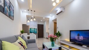 Un salon moderne avec un canapé gris, une table basse ornée d’un vase de fleurs, un téléviseur à écran plat et des luminaires suspendus.