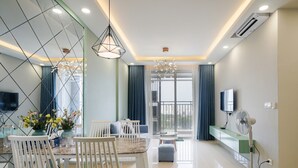 Un salon moderne comprenant un coin repas, un téléviseur et un balcon agrémenté de rideaux.