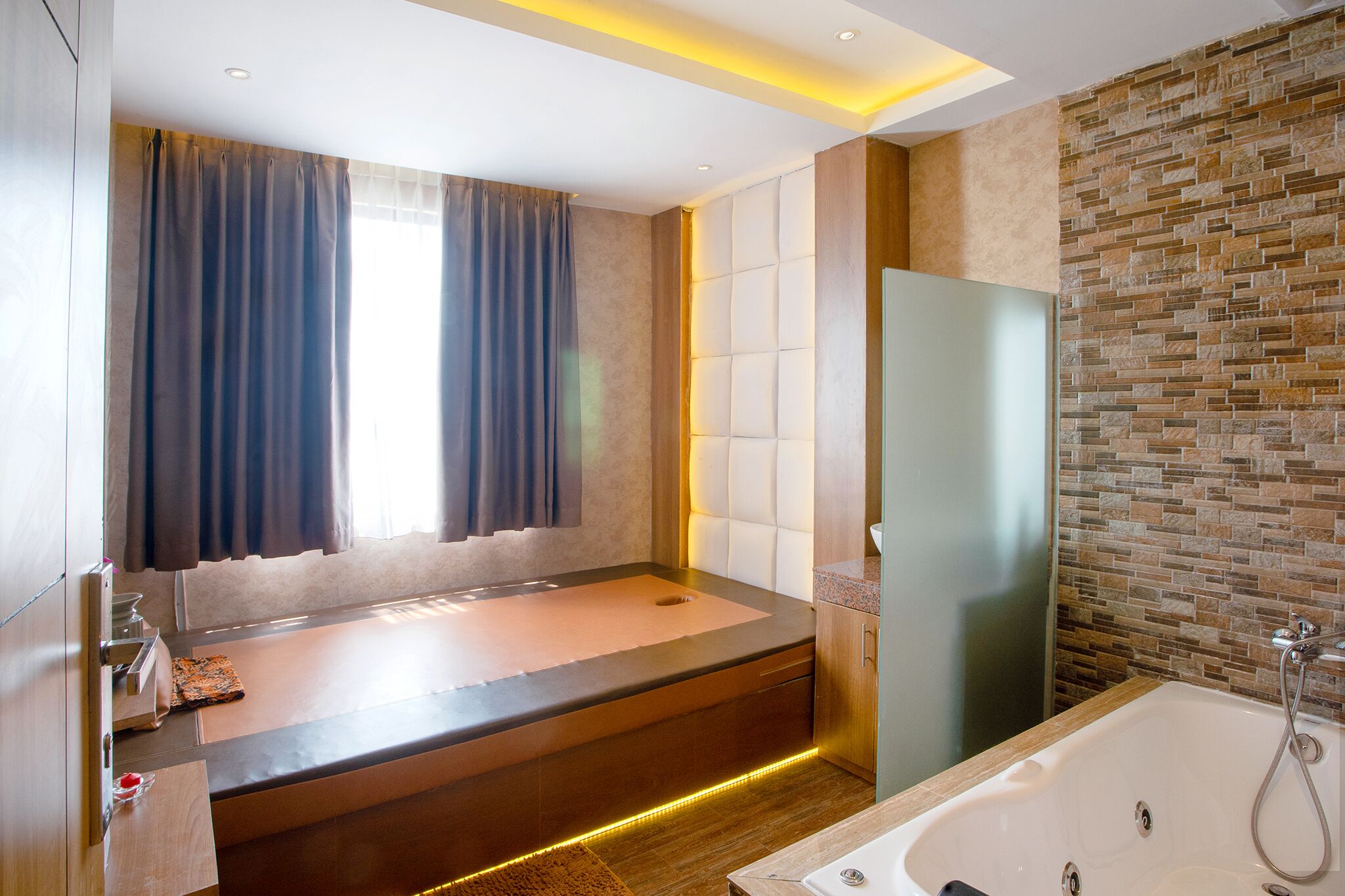 A modern bathroom with a large bathtub, a glass shower enclosure, and a stone mosaic wall.