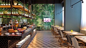 A restaurant with a tropical leaf wall, a buffet with various dishes, and a TV screen. - The Zuri Dumai (Dumai)