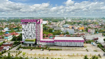 A modern hotel with a tall, pink and white facade, surrounded by a parking lot and a mix of residential and commercial buildings.