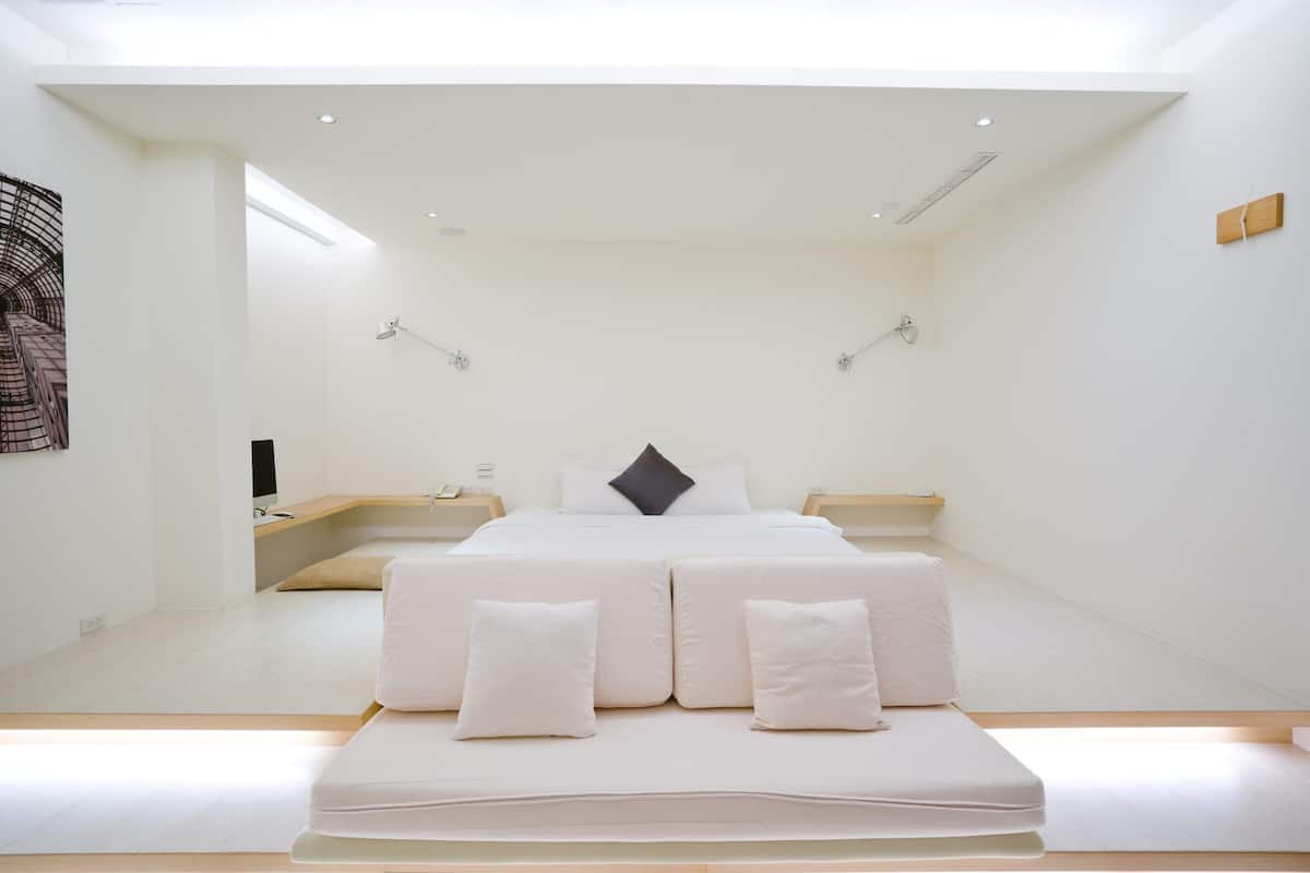 Una habitación de hotel minimalista con una cama grande, mesitas de noche y un escritorio pequeño.