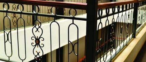 A metal railing with intricate designs, a beige wall, and a red floor.