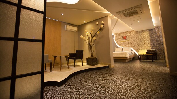 Habitación de hotel con diseño moderno, que incluye una cama, zona de estar y elementos decorativos como un jarrón con ramas.