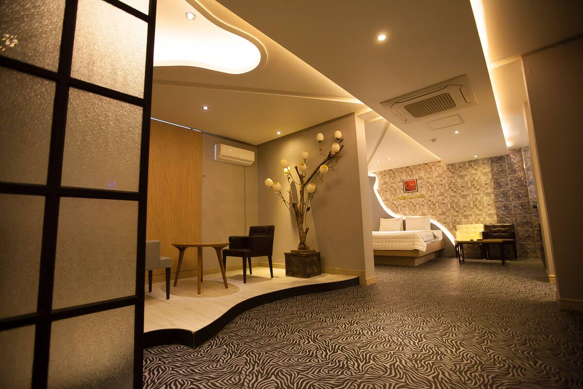 Habitació d'hotel amb un disseny modern, que inclou un llit, zona de seients i elements decoratius com un vas amb branques.