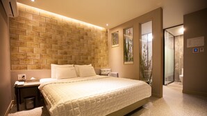 Habitación de hotel con una cama grande, una mesita de noche, un aire acondicionado instalado en la pared y un baño visible a través de una puerta abierta.