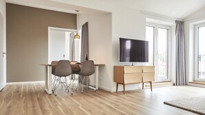 Una sala de estar moderna con comedor, un televisor de pantalla plana montado en la pared y ventanas amplias.
