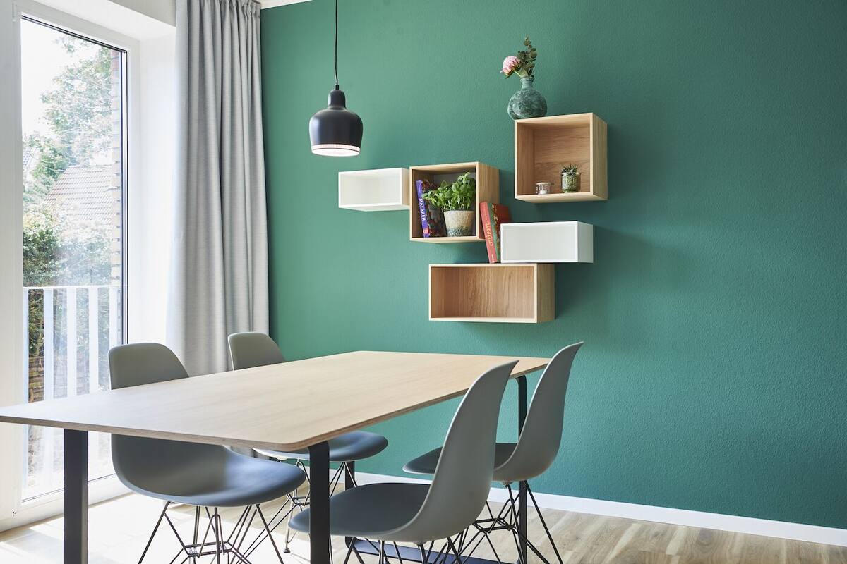 Un comedor con una mesa y sillas, una lámpara colgante y estanterías de pared con libros y objetos decorativos.