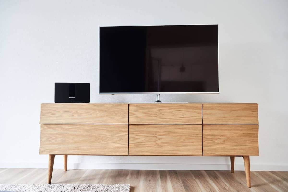 Un mueble de televisión moderno de madera con un televisor de pantalla plana y un altavoz negro.