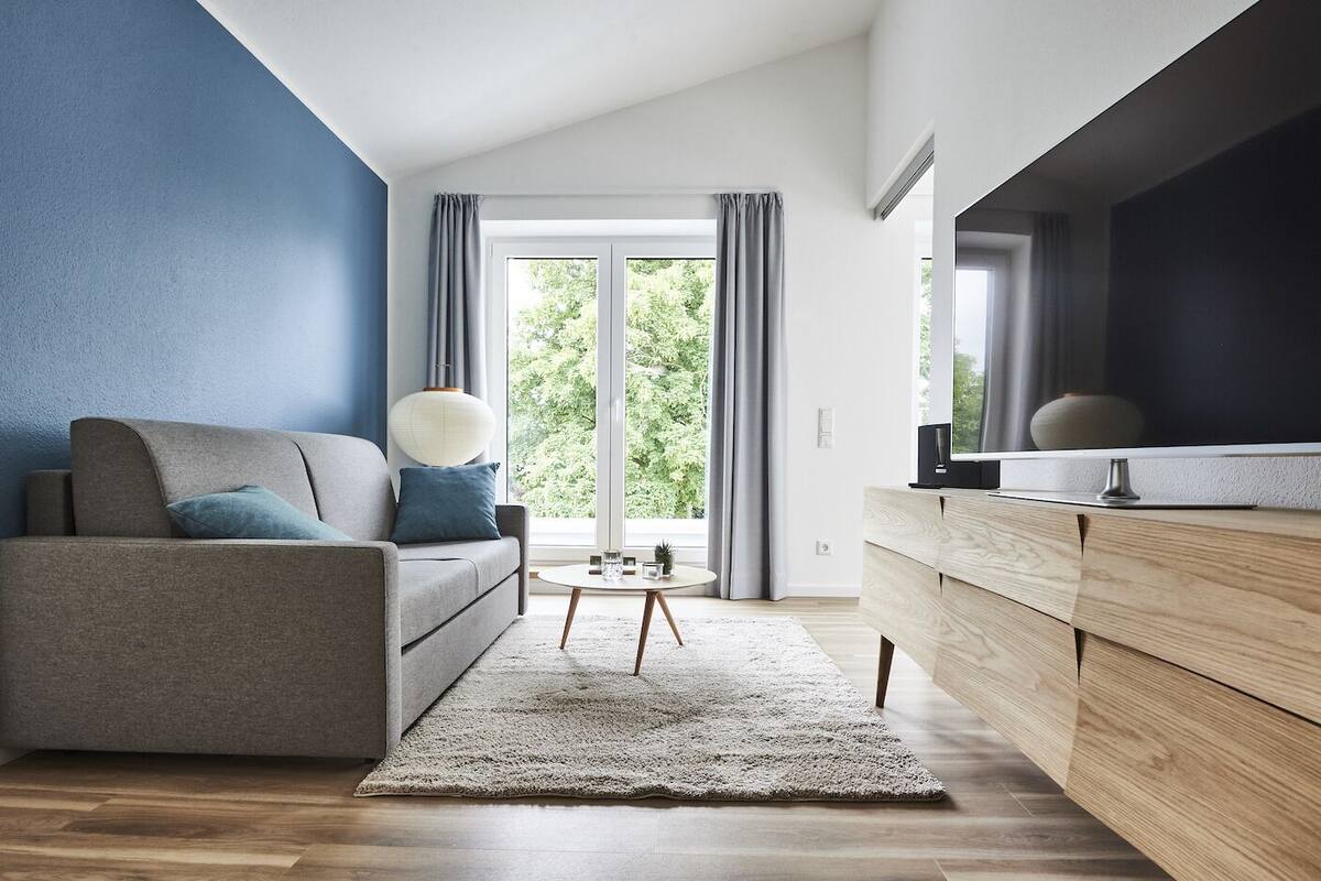 Una sala de estar moderna con un sofá gris, un aparador de madera y un ventanal con cortinas.