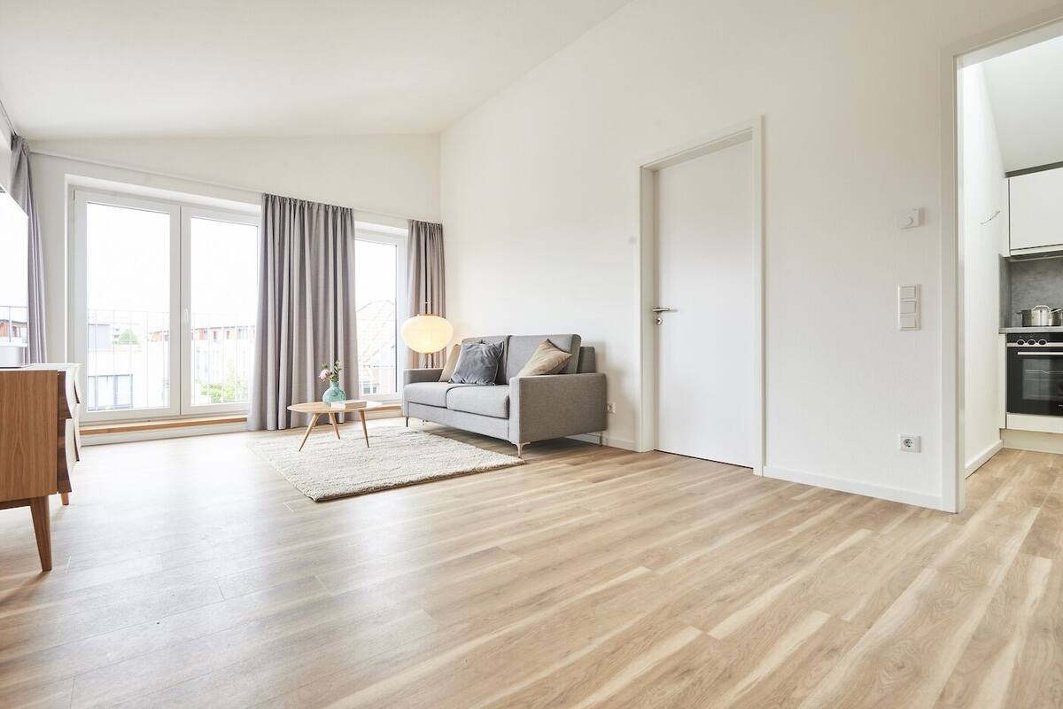 Un apartamento moderno con un sofá gris, una mesa de centro de madera y un ventanal con cortinas.