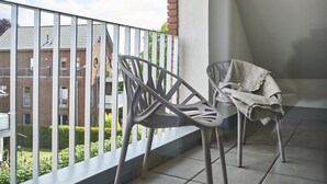 Un balcón con dos sillas y una mesa, vista a un edificio de ladrillo y una barandilla.