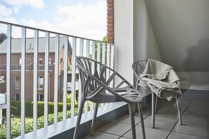Un balcón con dos sillas y una mesa, vista a un edificio de ladrillo y una barandilla.