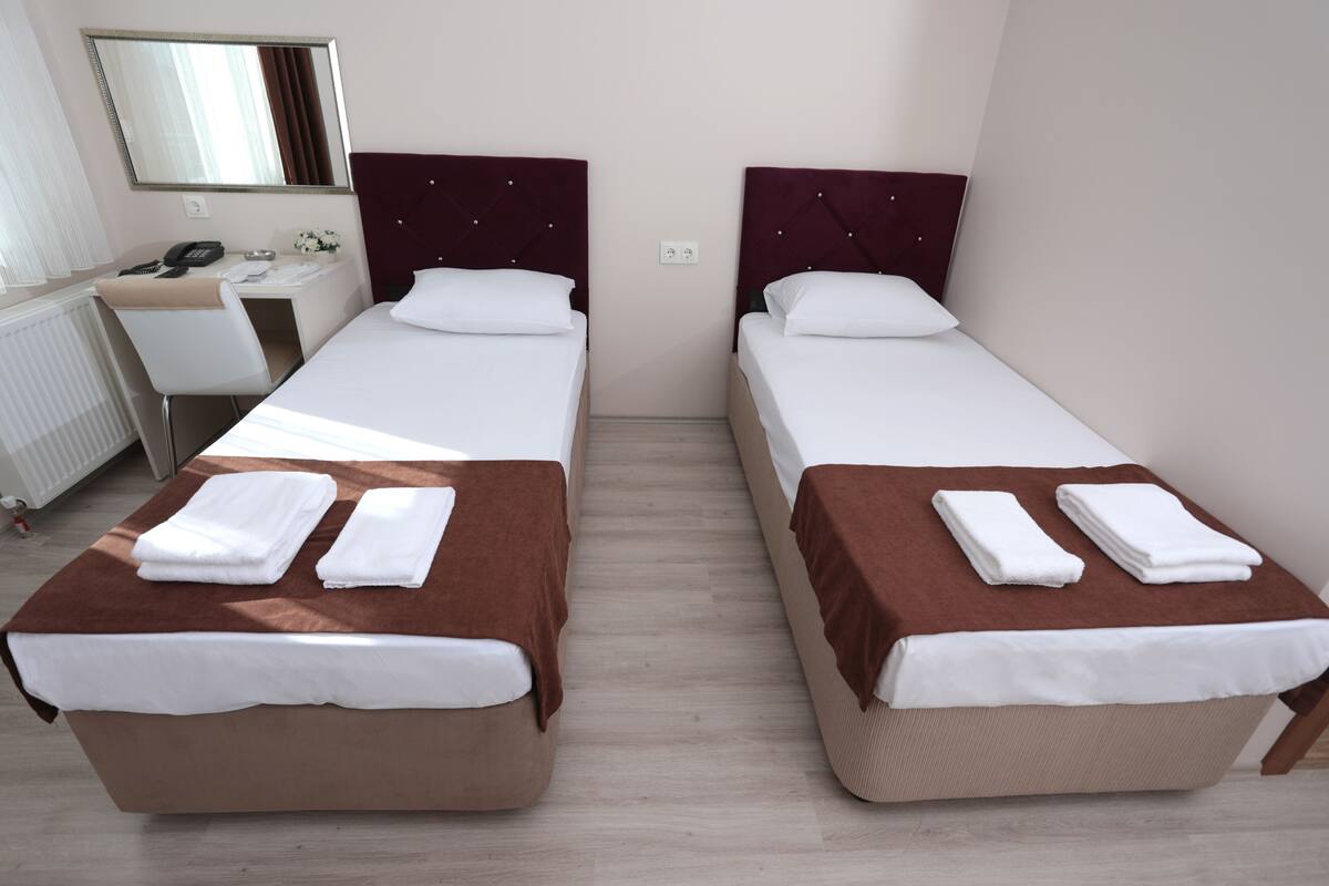 A hotel room with two single beds, a desk, a chair, and a mirror.
