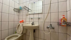 Een badkamer met toilet, wastafel en douche. Boven de wastafel hangt een spiegel en er is een plank met toiletartikelen.
