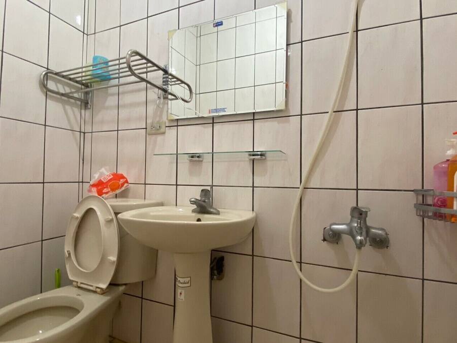 A bathroom with a toilet, sink, and shower. There is a mirror above the sink and a shelf with toiletries.