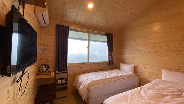 Een houten kamer met een bed, een televisie, een raam met gordijnen en een klein bureau met een waterkoker.